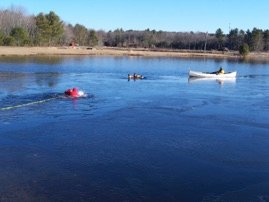 Rehoboth crews conducting a cold-water rescue drill on a pond, with a rescuer in the water and a boat standing by.